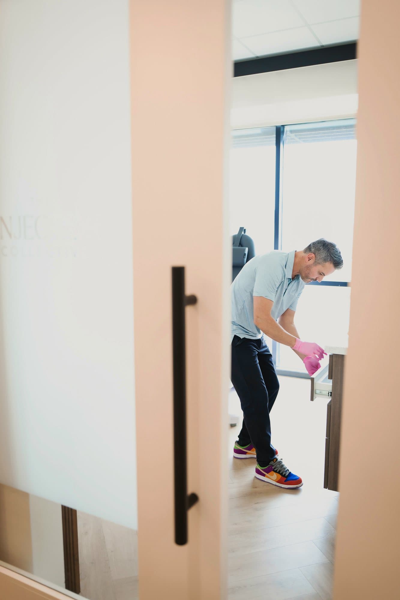 Through a frosted Injector Collective door, Ben Tracy, MD, at work inside a clinic room.